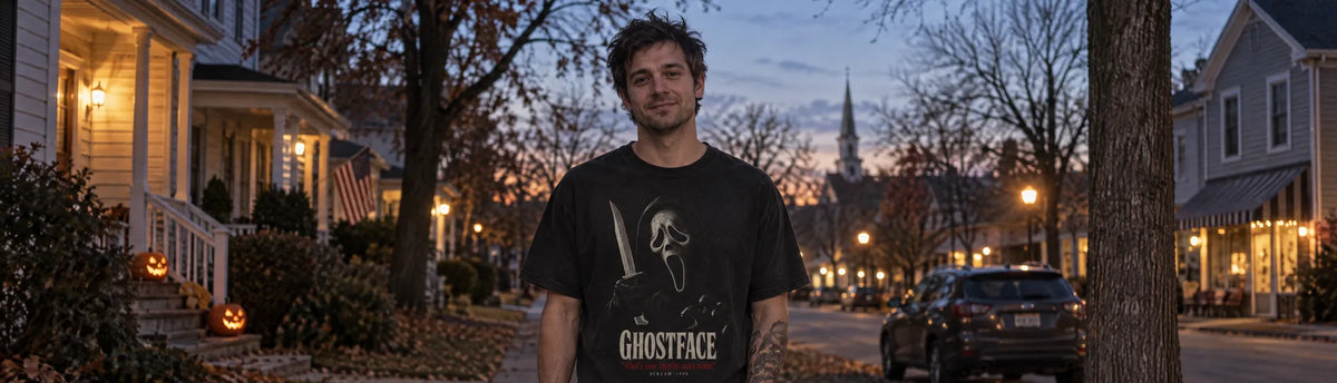 Man on a small-town street at dusk wearing the Cruel Royalty Ghostface Favorite Scary Movie graphic tee, jack-o'-lanterns on the porches